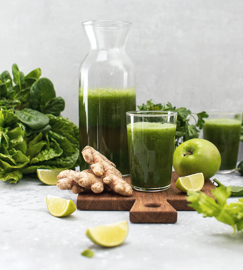 apples limes and ginger around a healthy smoothy and decanter on a cutting board